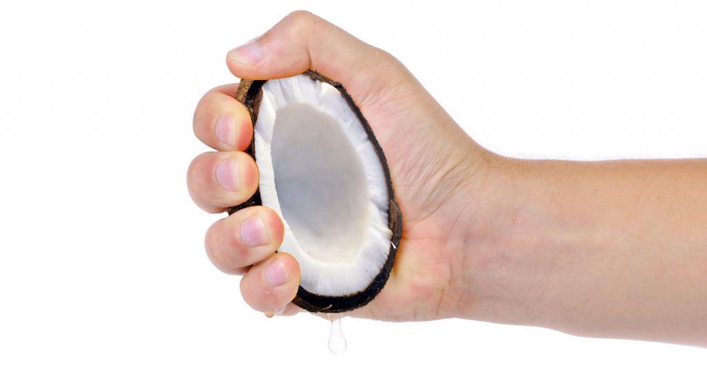 A hand squeezing coconut oil out of a half coconut